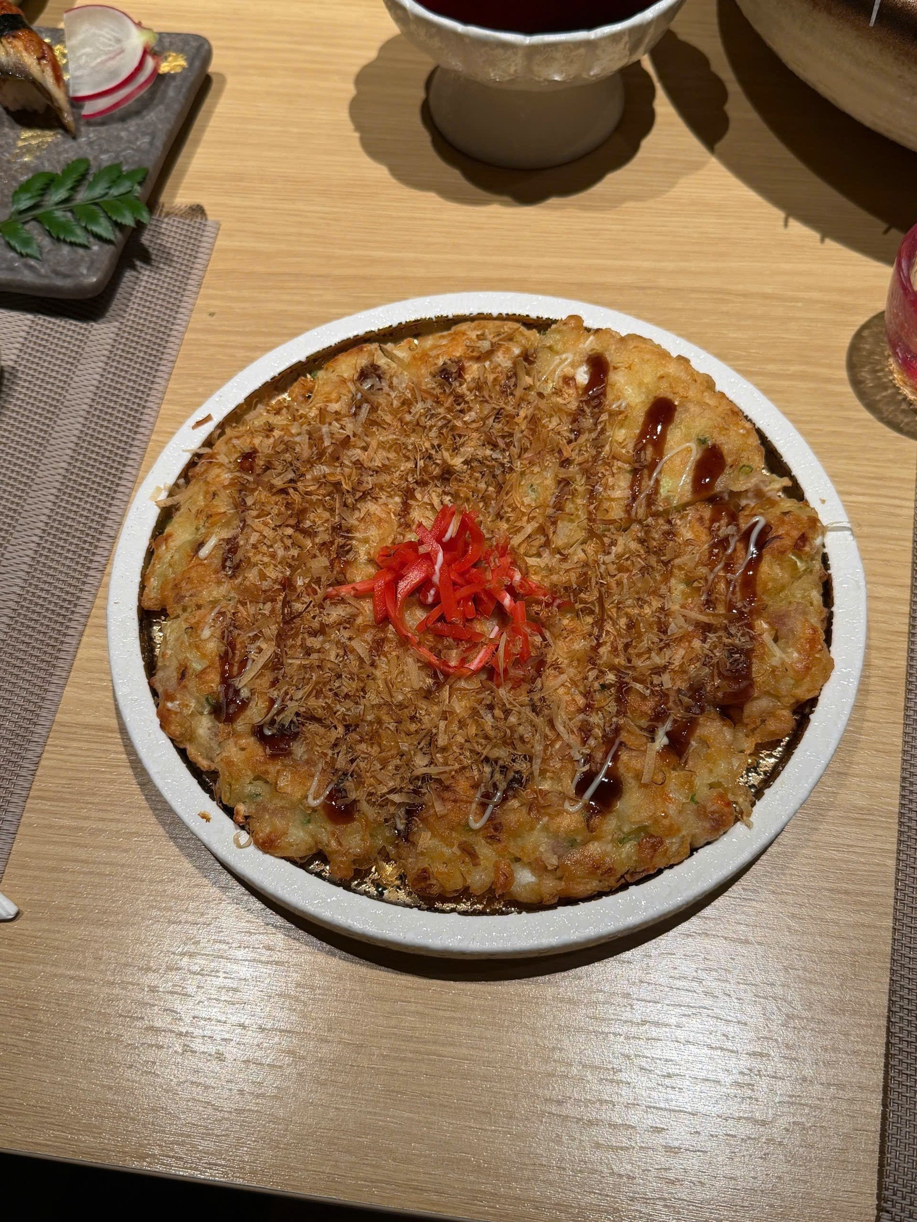 Okonomiyaki phủ cá bào, sốt, mayonnaise và gừng đỏ trên đĩa tròn
